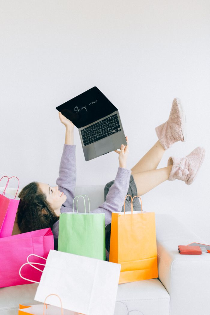 Home Woman lying on couch with laptop and colorful shopping bags, embodying online shopping joy.